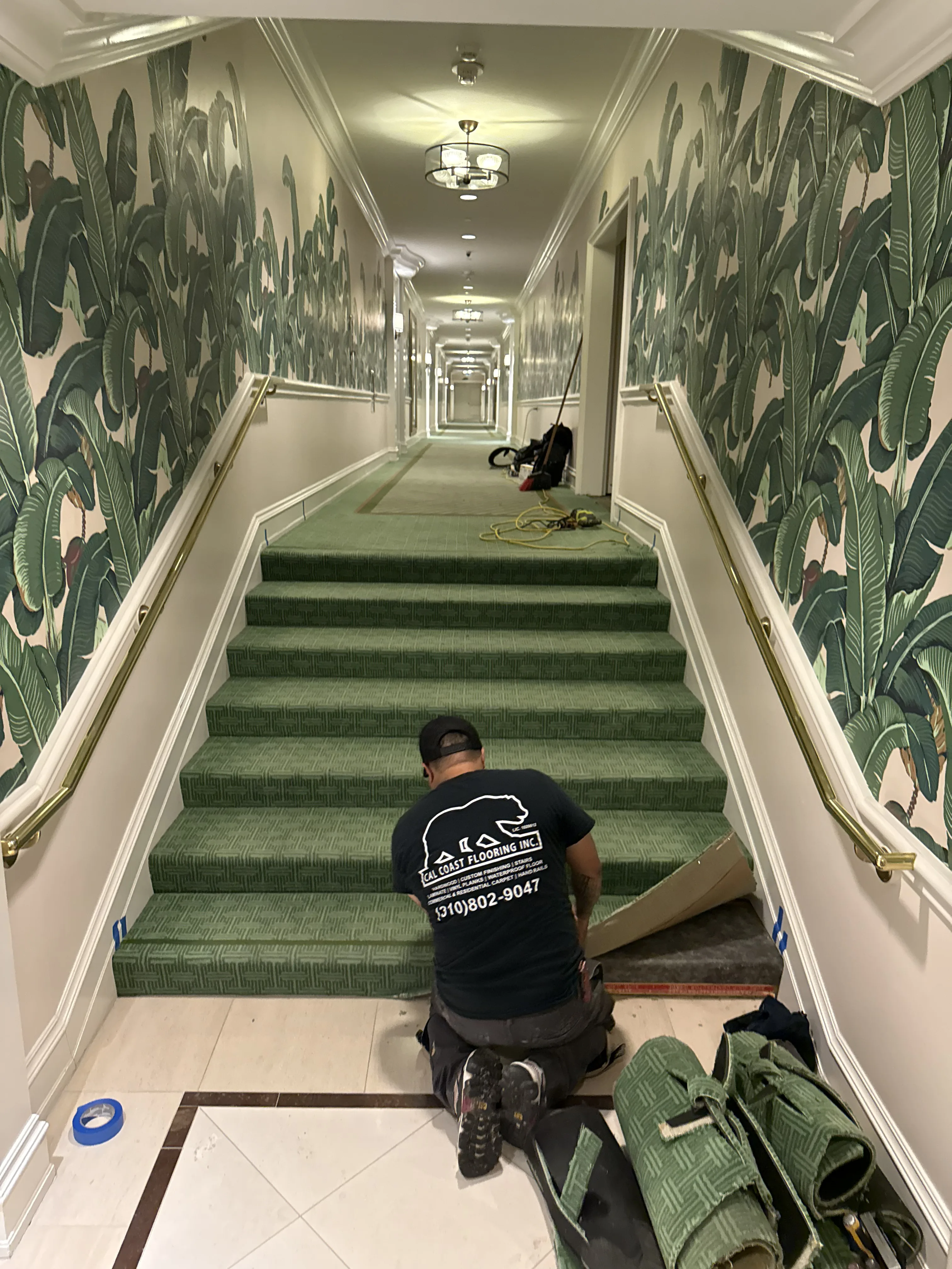 Cal Coast Flooring installer fitting a patterned green stair runner in a Beverly Hills Hotel hallway with banana-leaf wallpaper