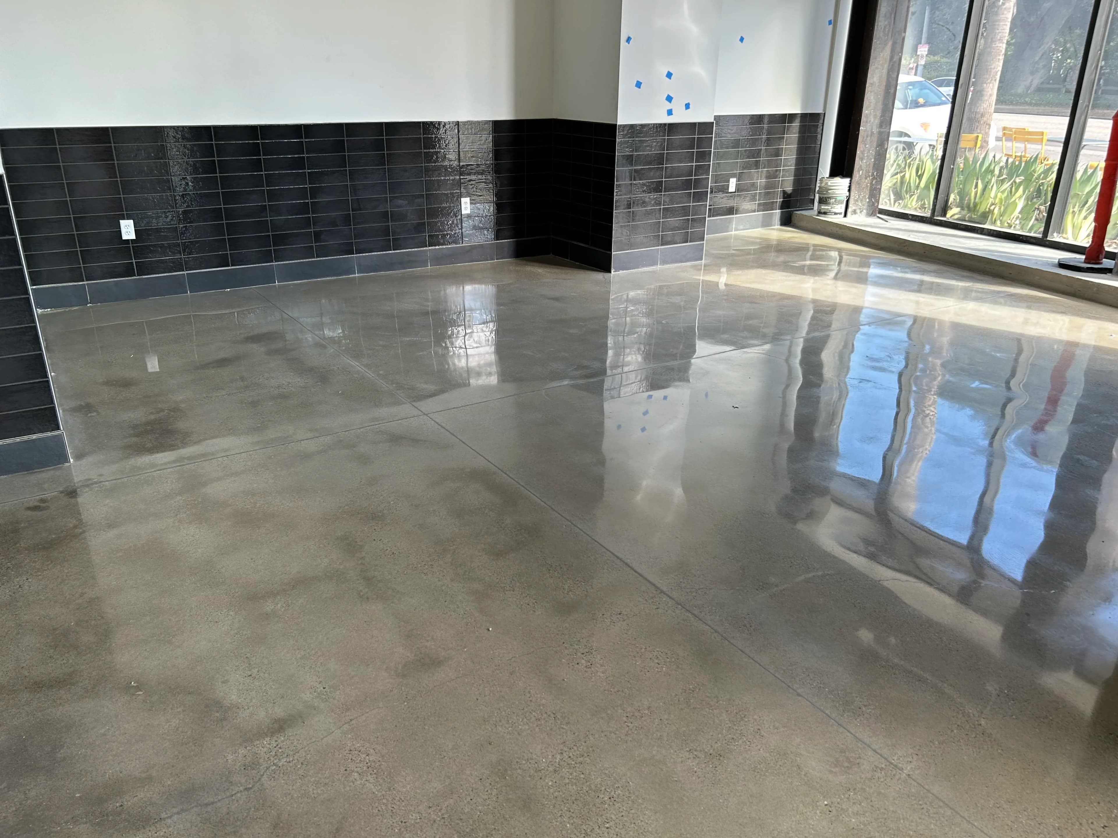 Polished concrete floor with high-gloss finish and black tile wainscot in a commercial space, finished by Cal Coast Flooring