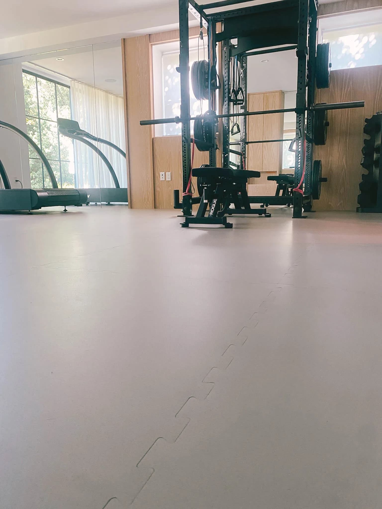 Home gym with interlocking rubber floor tiles, Rogue power rack, bench, and treadmill installed by Cal Coast Flooring