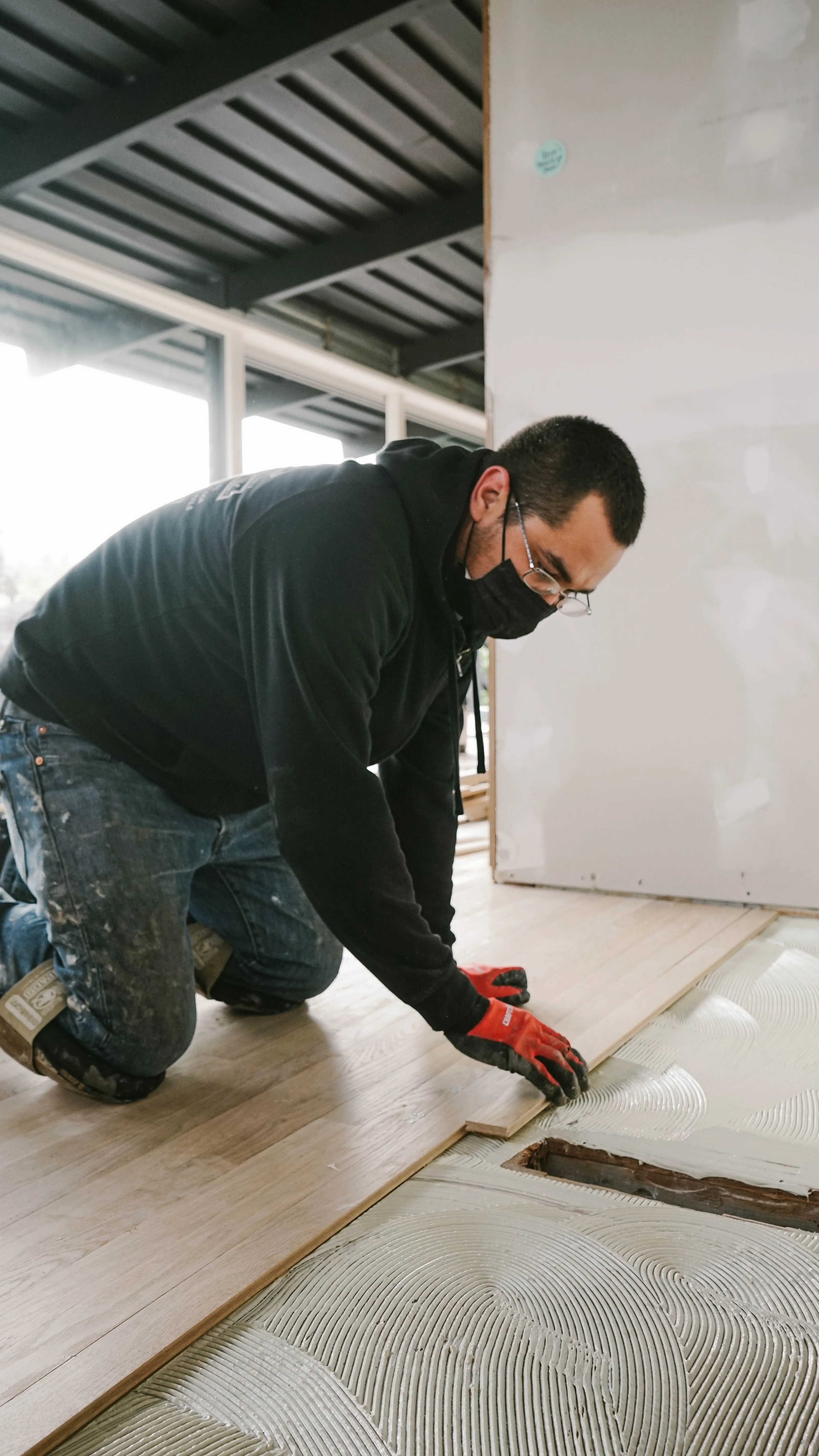 Cal Coast Flooring installer gluing down a white oak hardwood plank into a troweled adhesive bed on a commercial floor