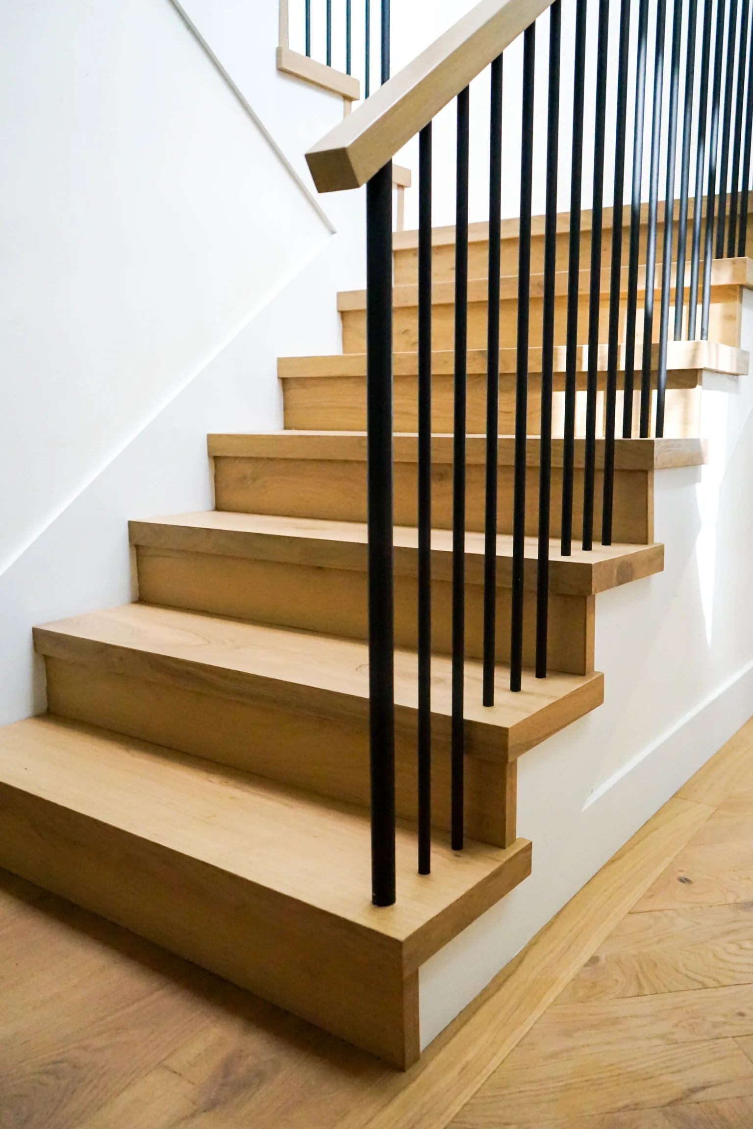Custom white oak box staircase with black metal spindle railing installed by Cal Coast Flooring, with herringbone oak floor at the base