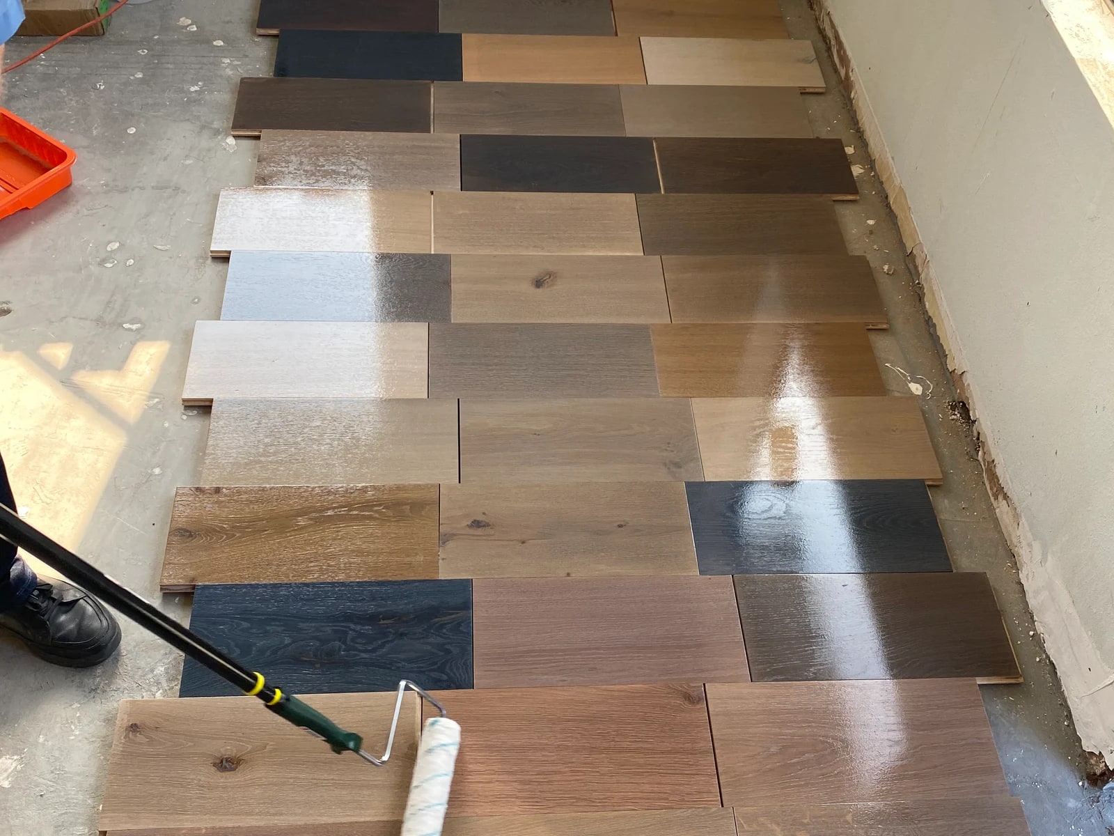 Rows of oak sample boards in reactive and custom stain colors laid out on a job-site floor, a roller applying the next coat