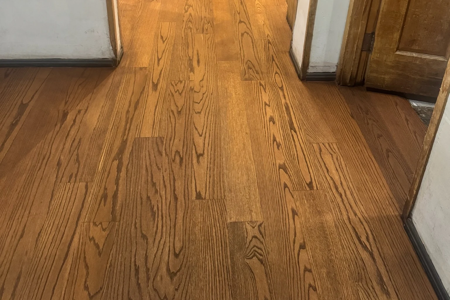 Red oak strip flooring in a warm stain running through a doorway, milled and installed by Cal Coast Flooring
